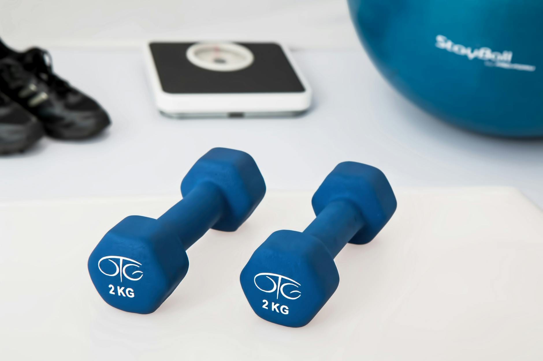 Niebieskie hantle na białym podłożu z rozmytym sprzętem fitness w tle